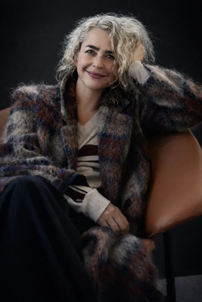 Retrato de Serena Ávila, sentada en un sillón de cuero con un abrigo de lana de cuadros